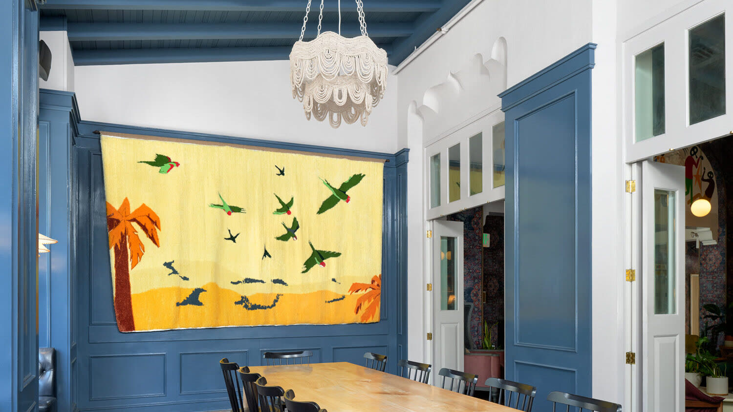 Default Cupertino, a large yellow tapestry of green parrots, installed in a blue-panelled dining room at The Graduate Berkeley